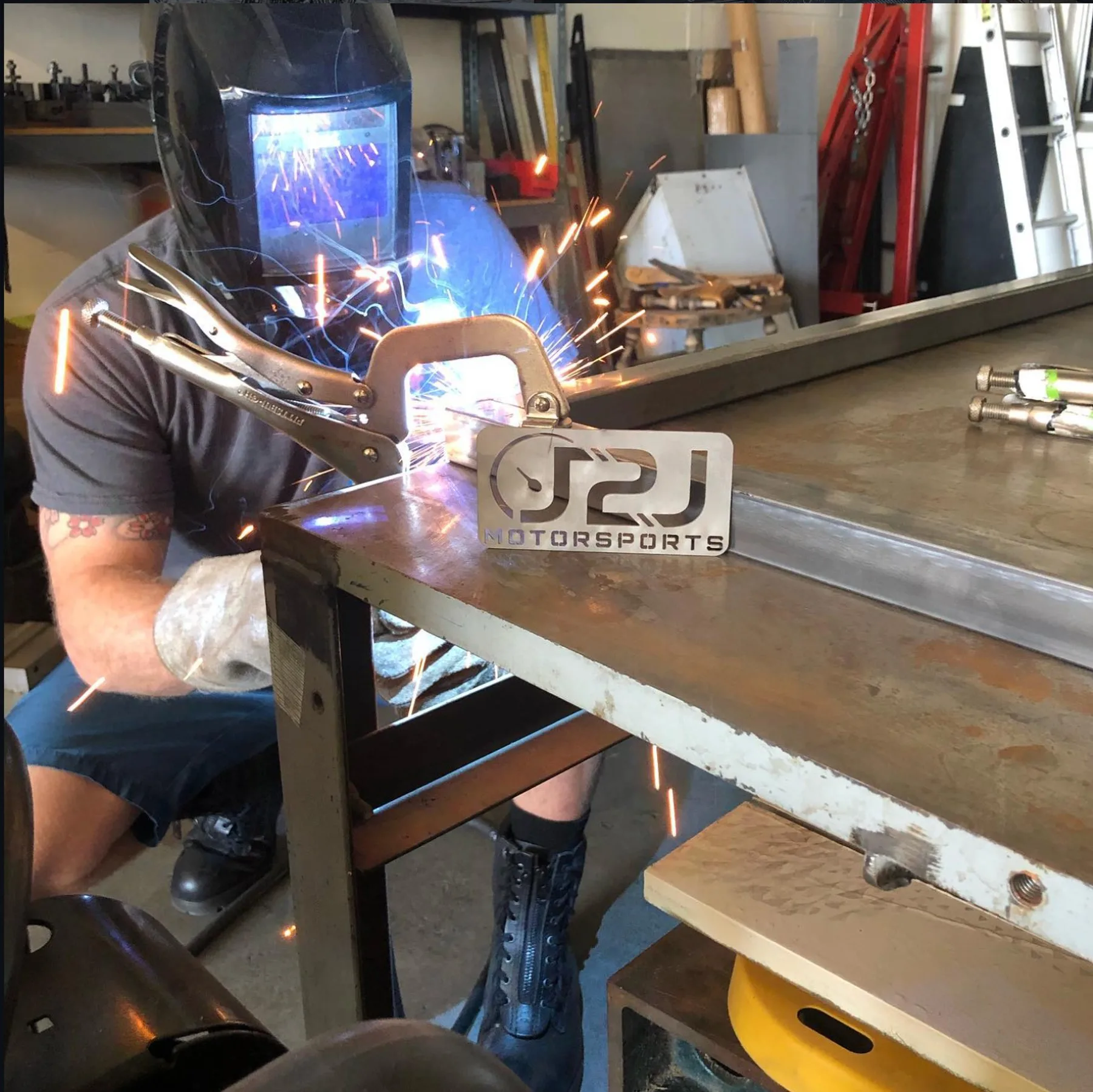 A mentor welding at the bench beside the J2J Motorsports shop sign